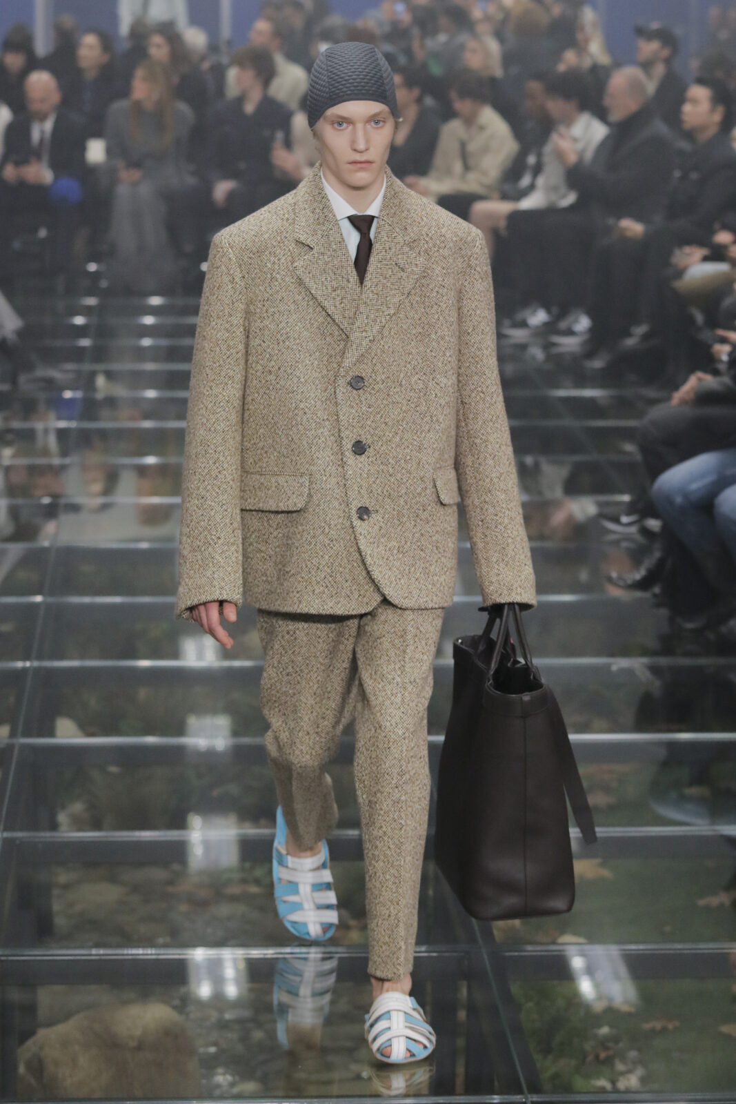 Prada model wearing a tailored suit and chore tweed coat on the runway