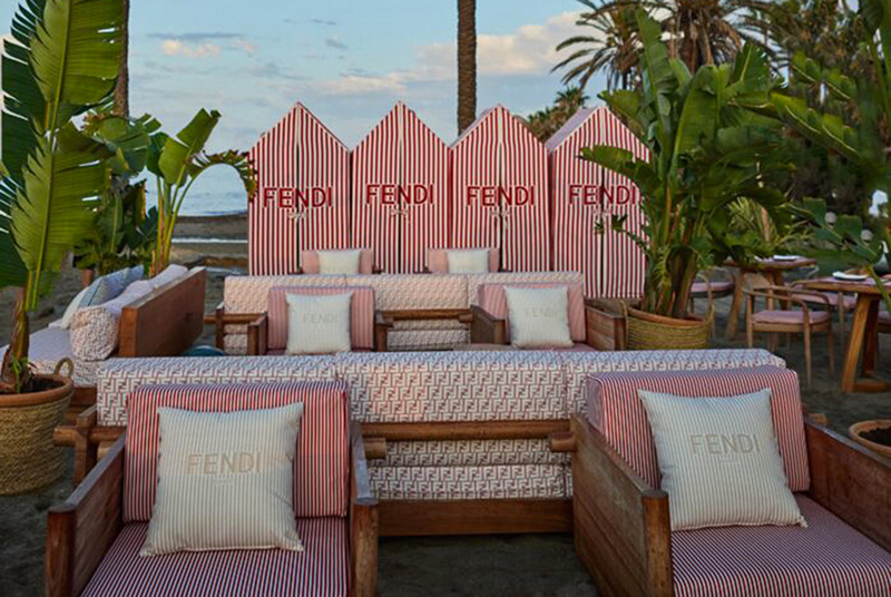 Lettini con cuscini rossi e gialli sotto ombrelloni monogram Fendi